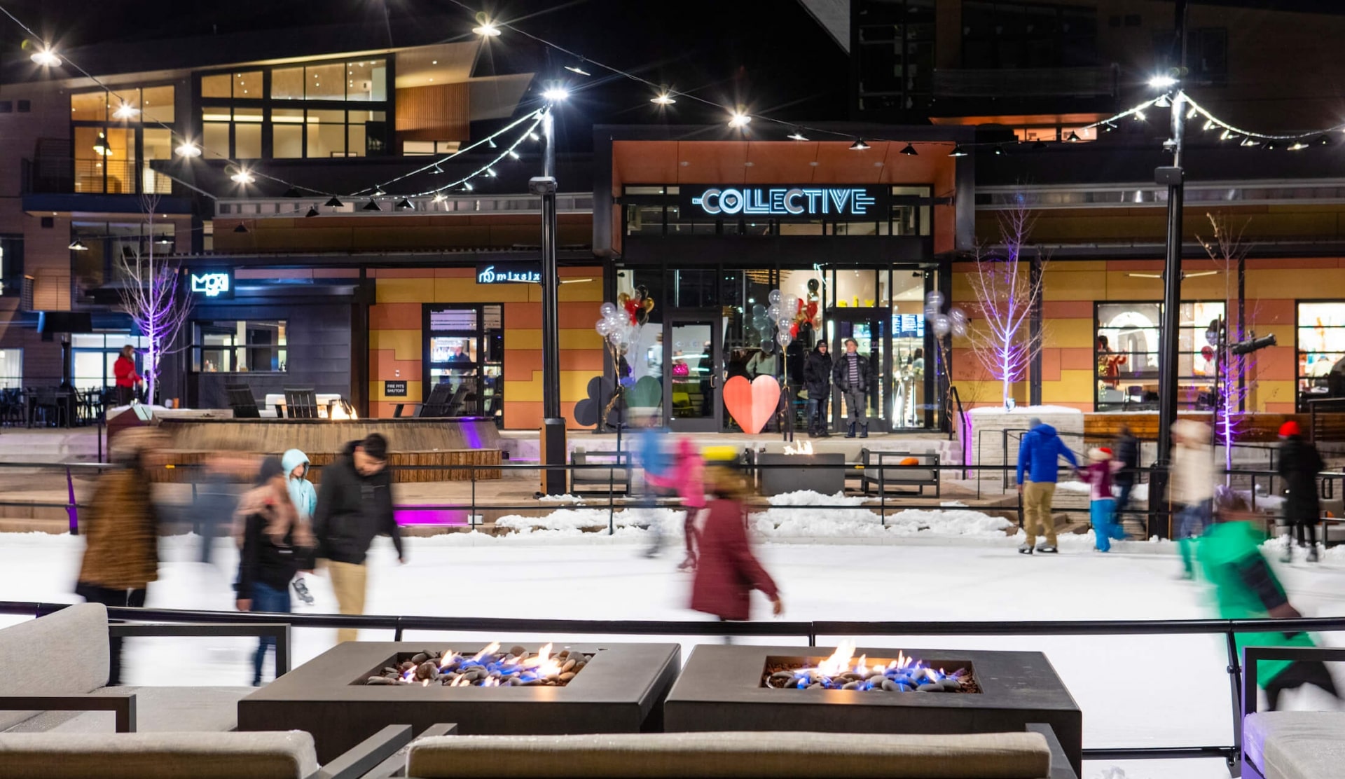 People ice skating at night under string lights and next to fire pits in Snowmass Base Village