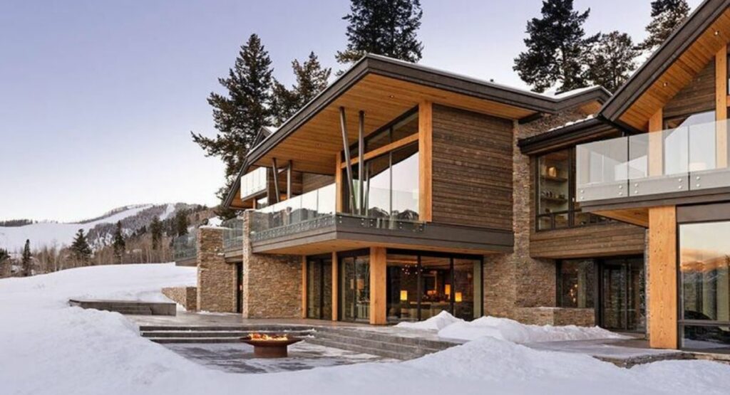 Modern Aspen vacation rental with easy ski-in ski-out access, surrounded by snow. A fire pit on the patio creates a warm, inviting atmosphere amidst the winter setting.
